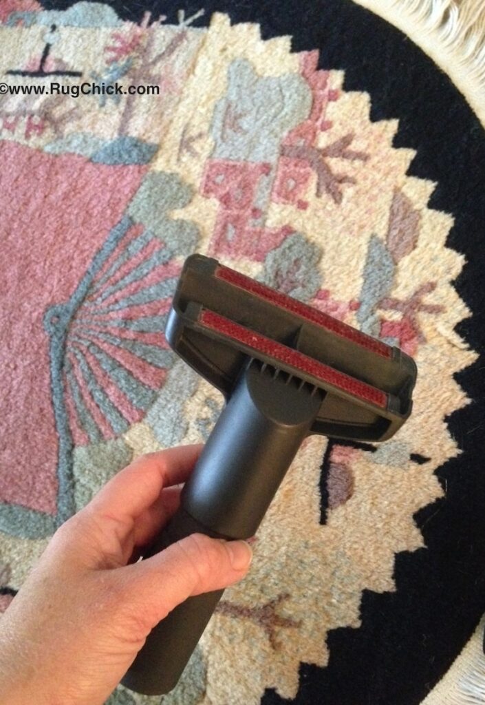 Using a handheld vacuum tool on a Moroccan wool rug to gently remove dust while protecting the fibers during regular rug maintenance.