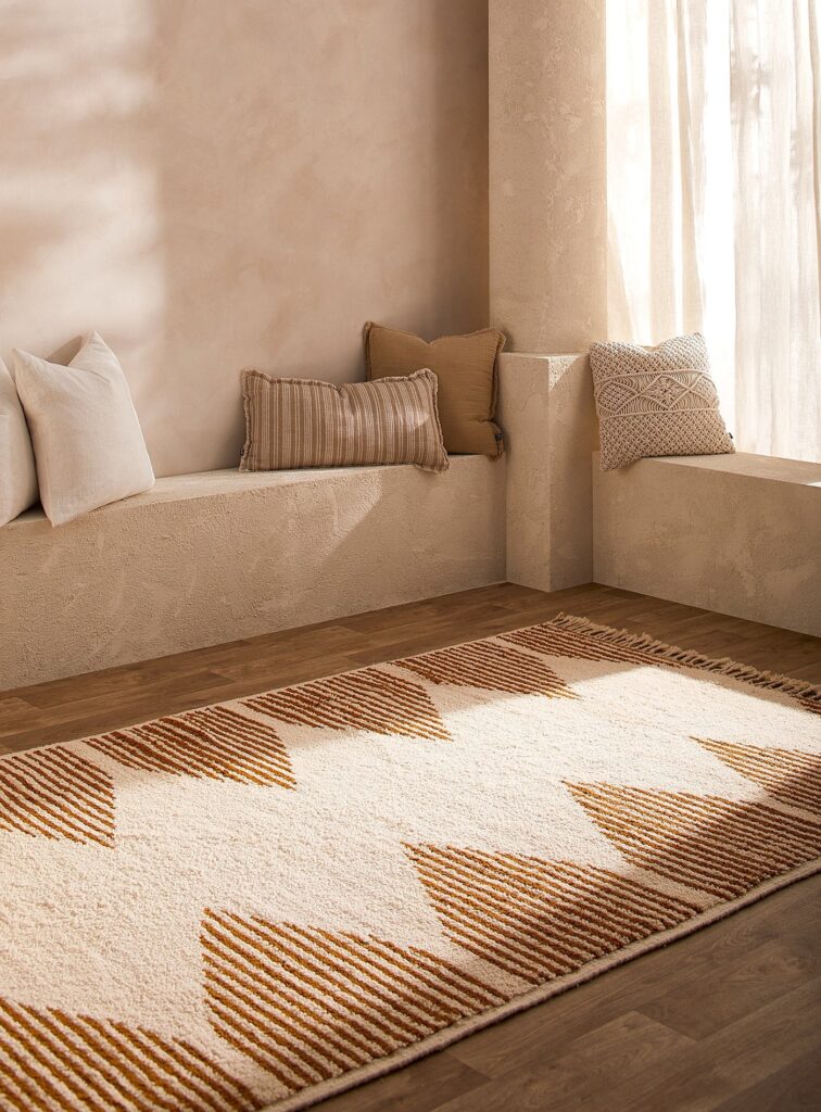 Handwoven Moroccan rug with geometric diamond patterns in warm beige and brown tones, placed in a minimalist interior to showcase texture and natural wool craftsmanship.