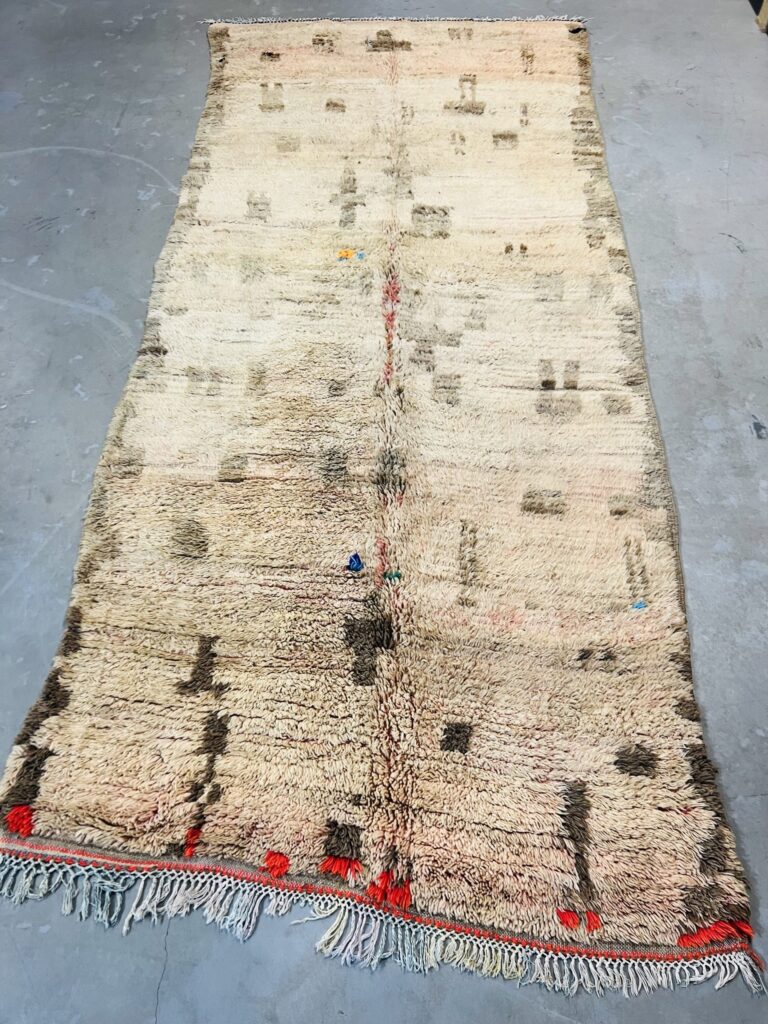 Vintage Moroccan Berber rug with thick wool pile and subtle abstract motifs in natural beige and brown tones, laid flat to show patina, texture, and traditional handwoven craftsmanship.
