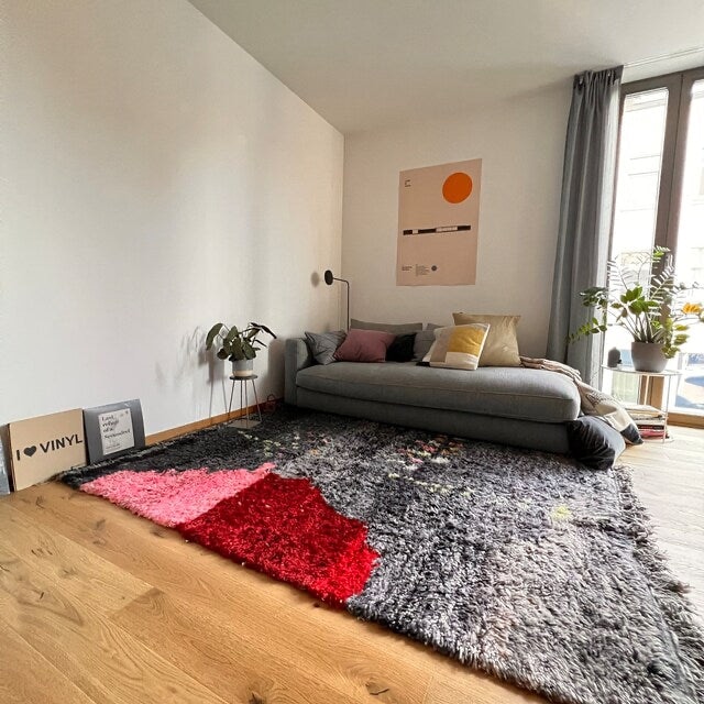 Handwoven Moroccan rug with thick shaggy wool and bold color blocks in gray, red, and pink, styled in a modern minimalist living room to highlight texture and contemporary appeal.