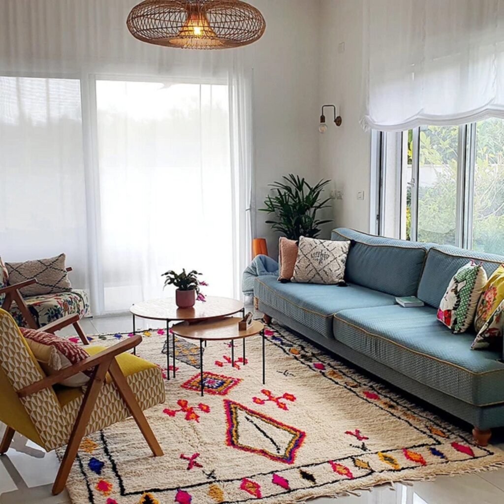 Handwoven Azilal rug with colorful abstract and geometric motifs, styled in a bright living room with a blue sofa, wooden furniture, and natural light to highlight Moroccan craftsmanship.