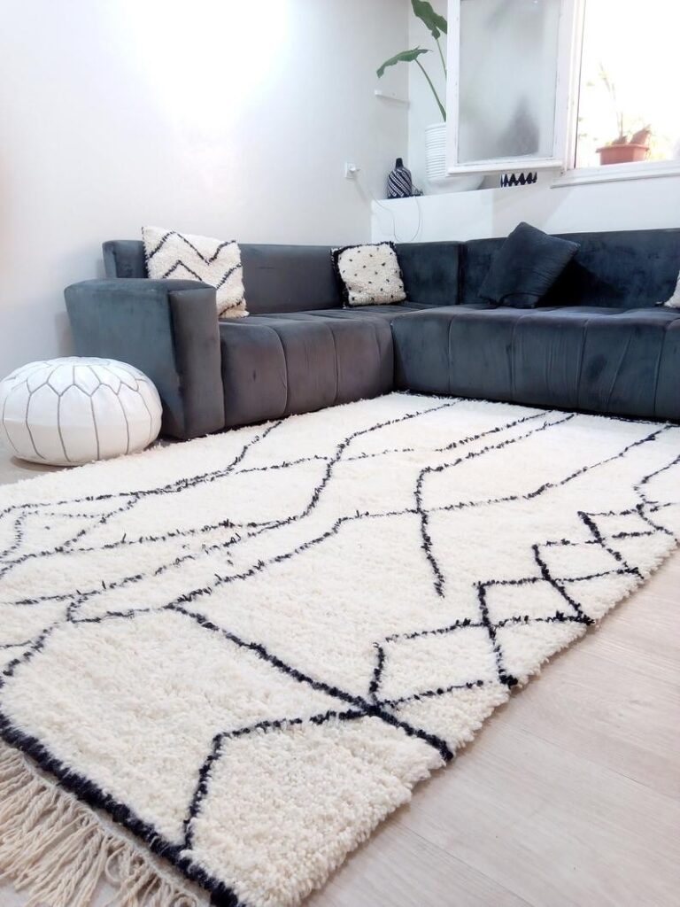 Authentic Beni Ourain rug with black geometric lines on ivory wool, styled in a modern living room with a dark sectional sofa.