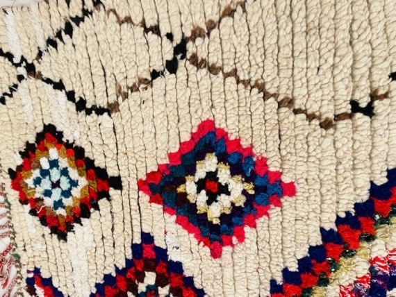 Close-up of a handwoven Moroccan rug showing colorful diamond motifs on an ivory wool background, highlighting thick pile texture and traditional craftsmanship.