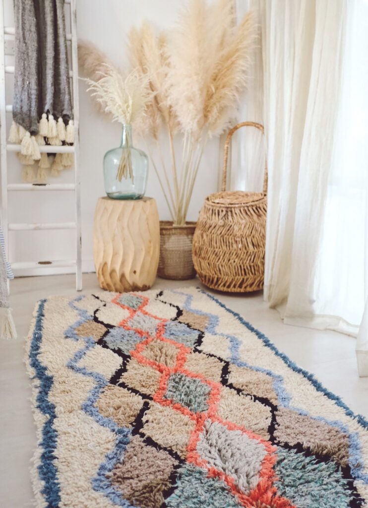 Handwoven Moroccan rug with soft geometric patterns in beige, blue, and coral tones, styled in a light-filled interior with natural decor elements to highlight texture and warmth.