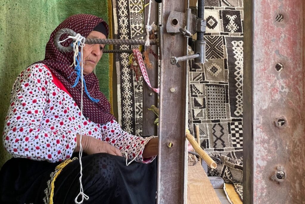 Moroccan artisan woman handweaving a traditional Beni Ourain rug on a vertical loom using natural wool.
