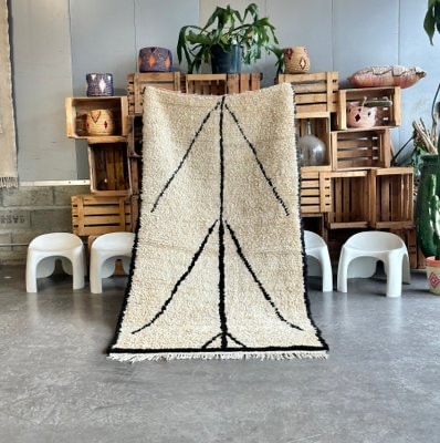 Handwoven Moroccan rug with minimalist black linear motifs on an ivory wool base, displayed indoors to highlight texture, simplicity, and traditional craftsmanship.