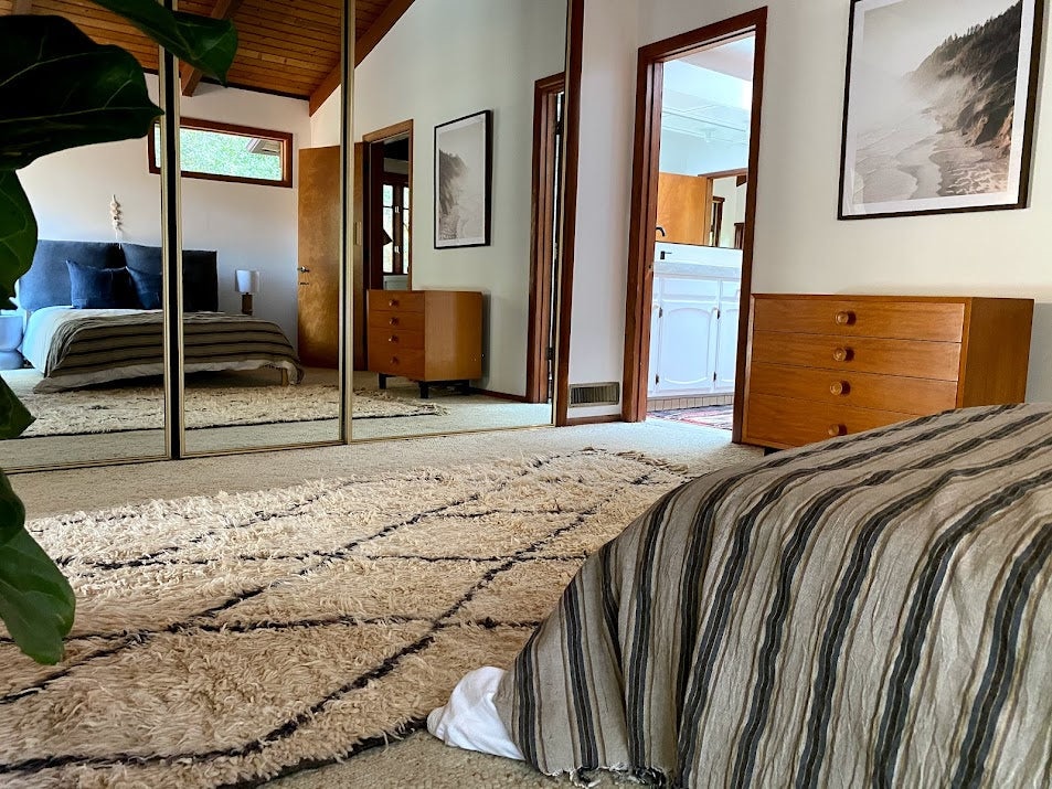 Bedroom interior featuring an authentic Beni Ourain rug with subtle black lines on ivory wool, placed beside a bed in a warm, minimalist space.