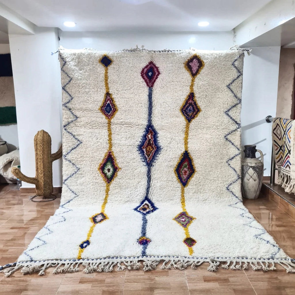Handwoven Azilal rug with ivory wool base and colorful diamond motifs in blue, yellow, and red, displayed indoors to highlight texture and traditional Moroccan craftsmanship.