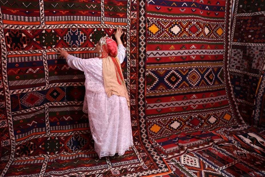 Berber woman inspecting a handwoven Moroccan Tazenakht rug with bold geometric patterns and natural dyes