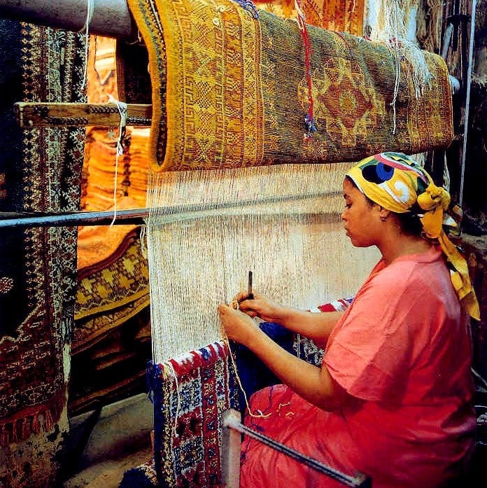 Moroccan artisan handweaving a traditional wool rug on a loom, showcasing ancestral rug-making techniques and colorful patterns.