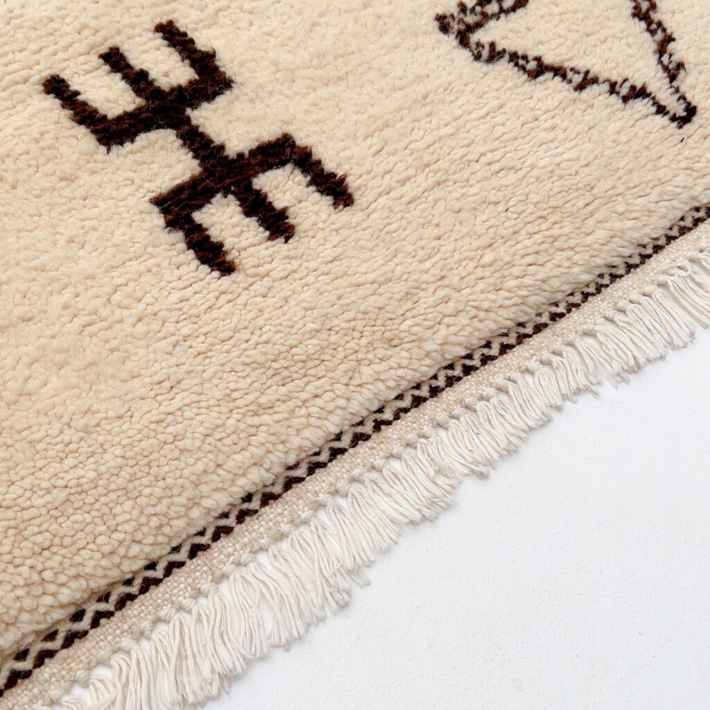 Close-up of an authentic Beni Ourain rug showing dark brown geometric symbols on ivory wool with hand-knotted fringe.