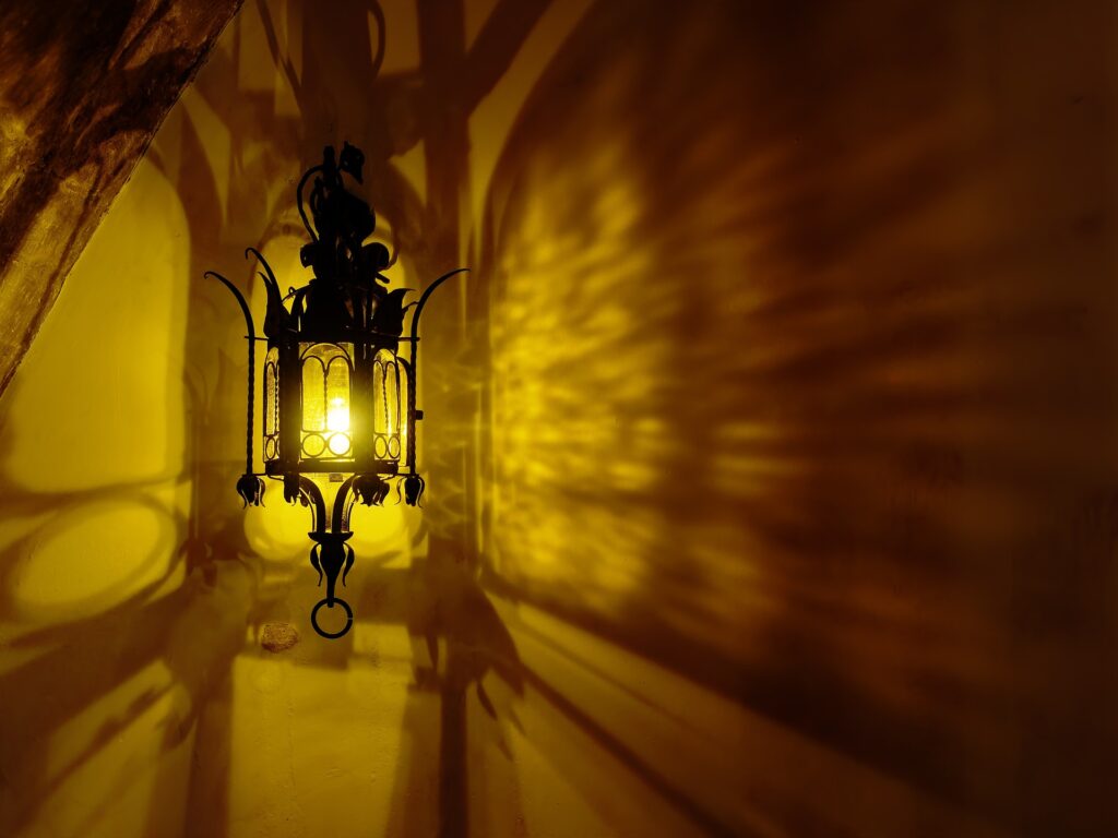 Moroccan metal lantern casting dramatic shadows on a yellow wall, creating warm ambient lighting.