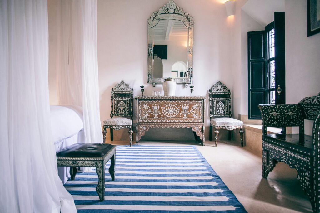 Elegant Moroccan bedroom with carved wood inlay furniture, striped rug, and canopy bed.