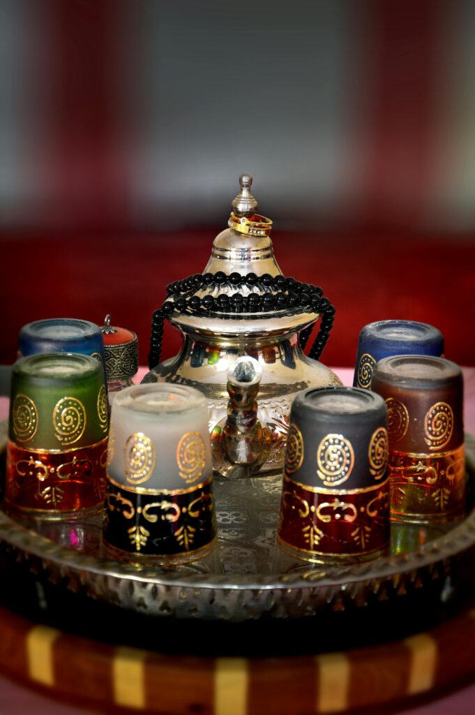 Traditional Moroccan silver tea pot and colorful decorated tea glasses arranged on a metal tray.