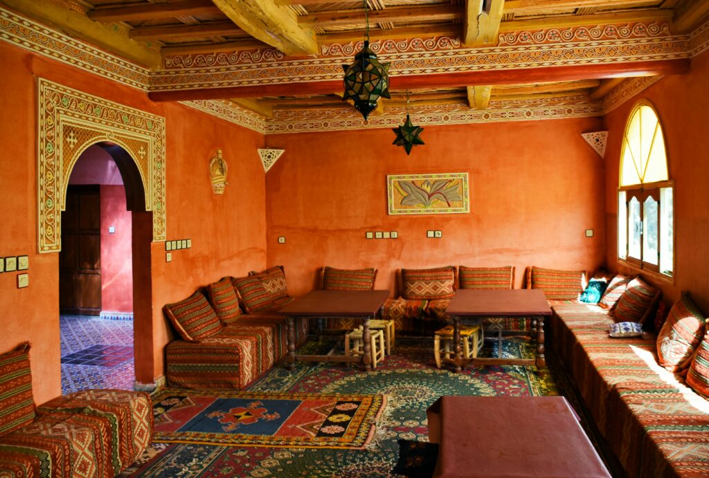 Traditional Moroccan living room with terracotta walls, patterned cushions, low wooden tables, and Berber rugs.