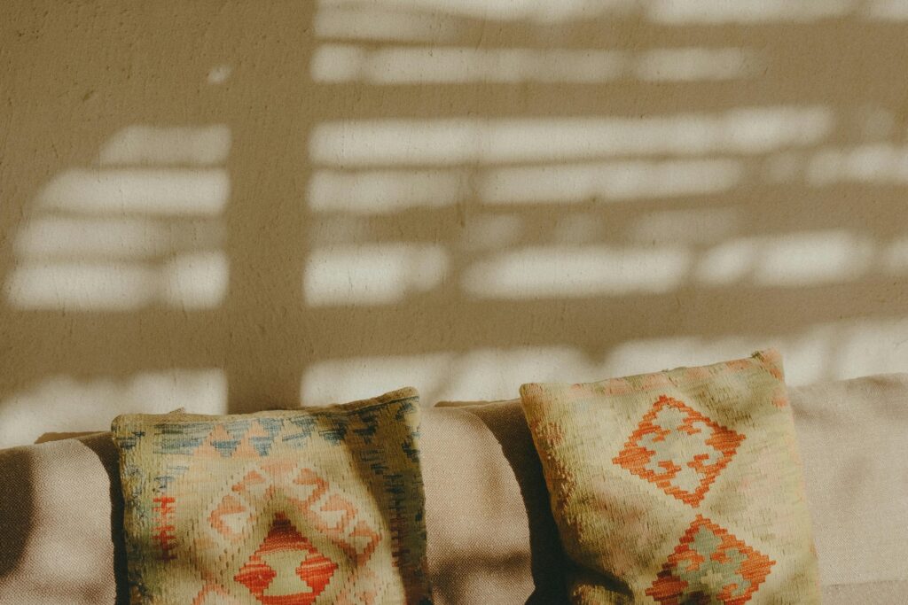 Moroccan patterned cushions on a neutral sofa with warm desert sunlight casting shadows on the wall.
