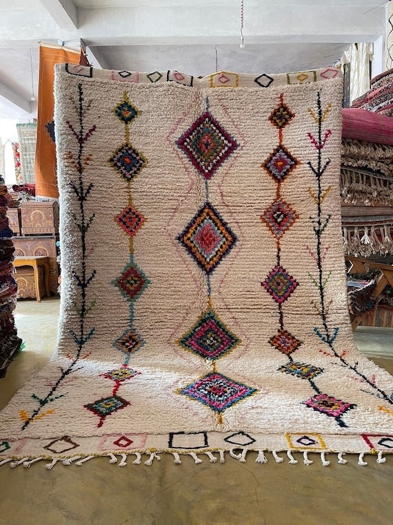 Handwoven Azilal rug with ivory wool base and colorful diamond motifs arranged in vertical lines, displayed indoors to showcase texture and traditional Moroccan craftsmanship.