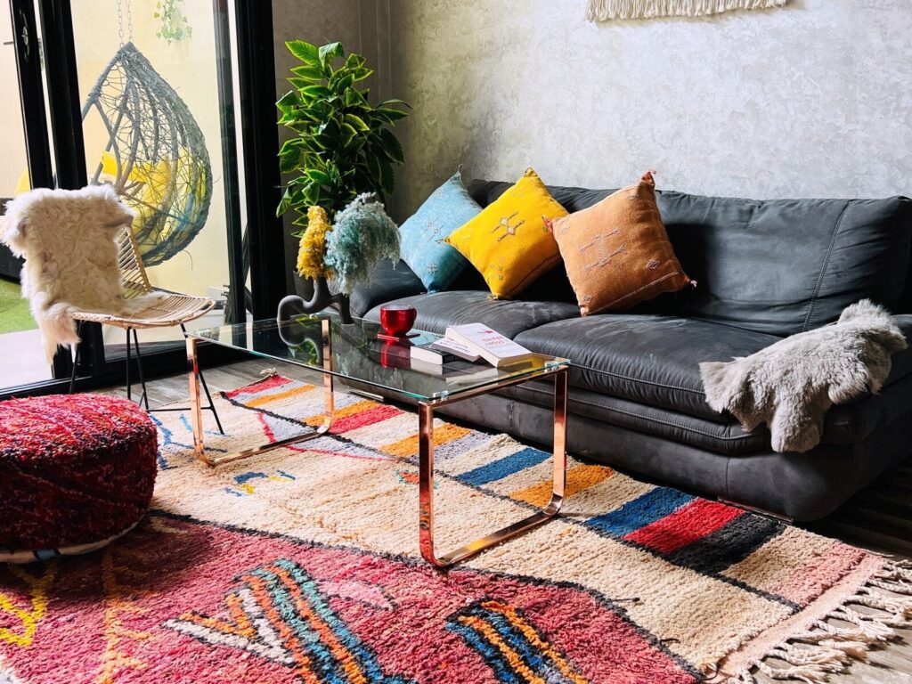 Colorful Moroccan Beni Ourain rug with geometric patterns, styled in a modern living room with a dark sofa, glass coffee table, and textured cushions.