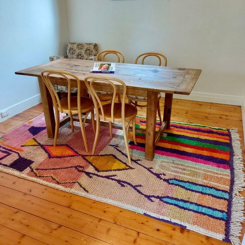 Colorful handwoven Moroccan rug with abstract geometric patterns, placed under a wooden dining table to show how an Azilal-style rug adds warmth and character to a dining space.