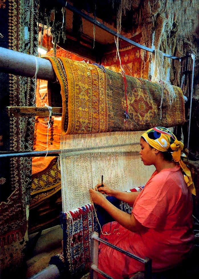 Moroccan artisan weaving a traditional rug on a hand loom, showing the craftsmanship, tools, and techniques behind handmade Berber rugs.