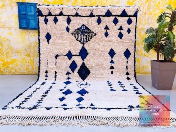 Authentic Beni Ourain rug with blue geometric diamond patterns on natural ivory wool, handwoven in Morocco and displayed in a bright interior.