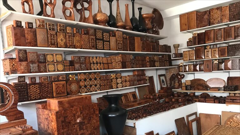 Shelves filled with handmade Thuya wood marquetry boxes and decorative objects in an Essaouira workshop, showing natural grain variations and traditional Moroccan patterns.