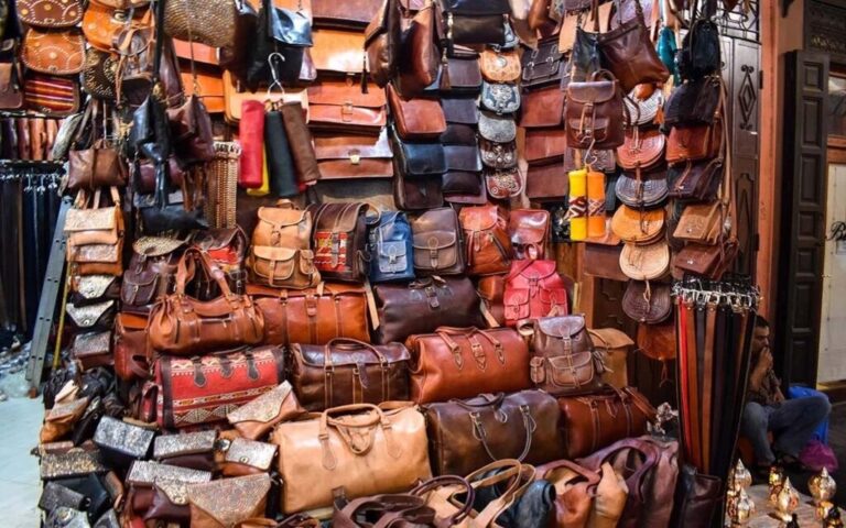 Authentic Moroccan leather bags displayed in a traditional souk, showing handmade satchels, backpacks, and duffel bags in natural vegetable-tanned leather.