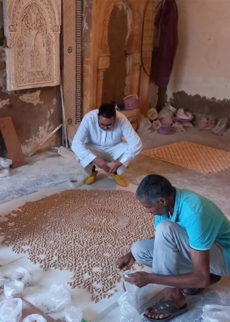 Moroccan artisans working by hand on a traditional mosaic floor, carefully placing individual pieces in a workshop setting.